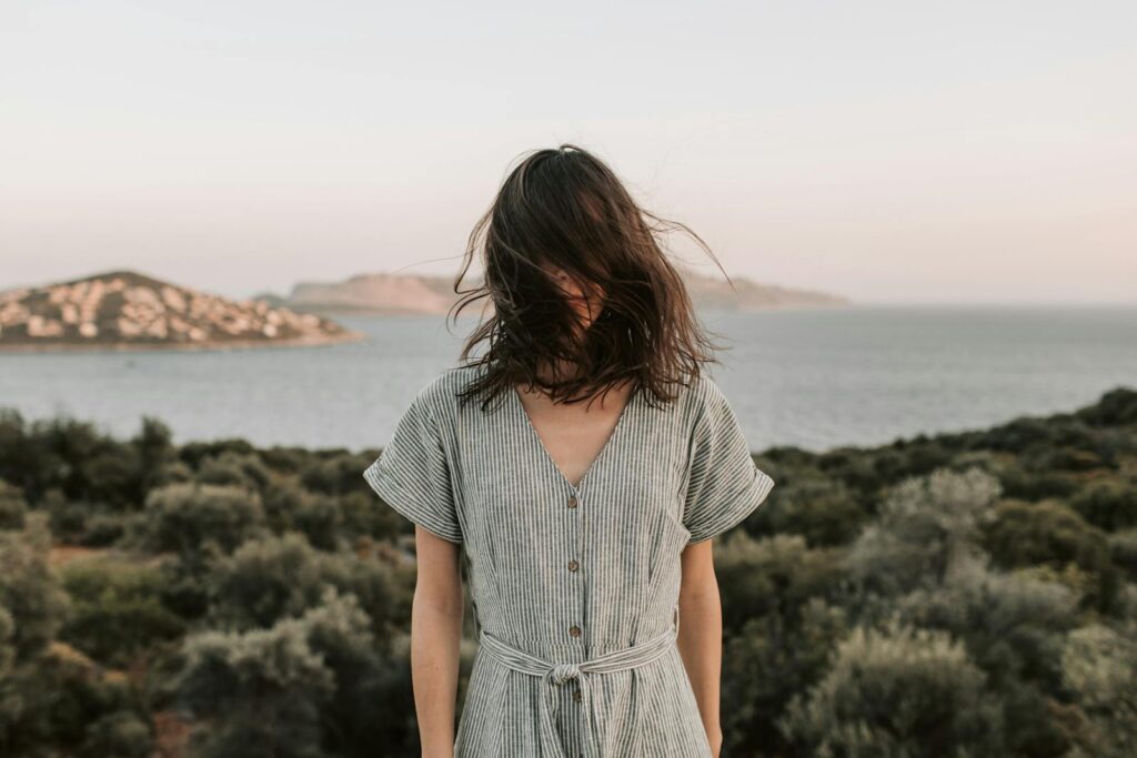 A woman with hair blown by wind stands by the serene Antalya coast at sunset, capturing summer's essence.