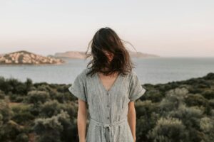 A woman with hair blown by wind stands by the serene Antalya coast at sunset, capturing summer's essence.