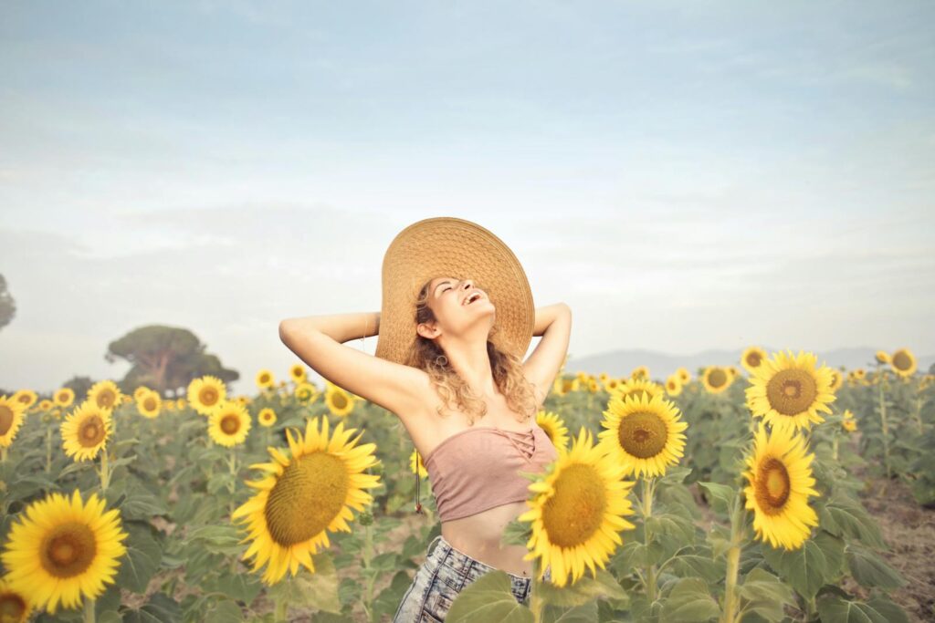 A woman in a sunflower field, embracing nature with joy under the summer sun.